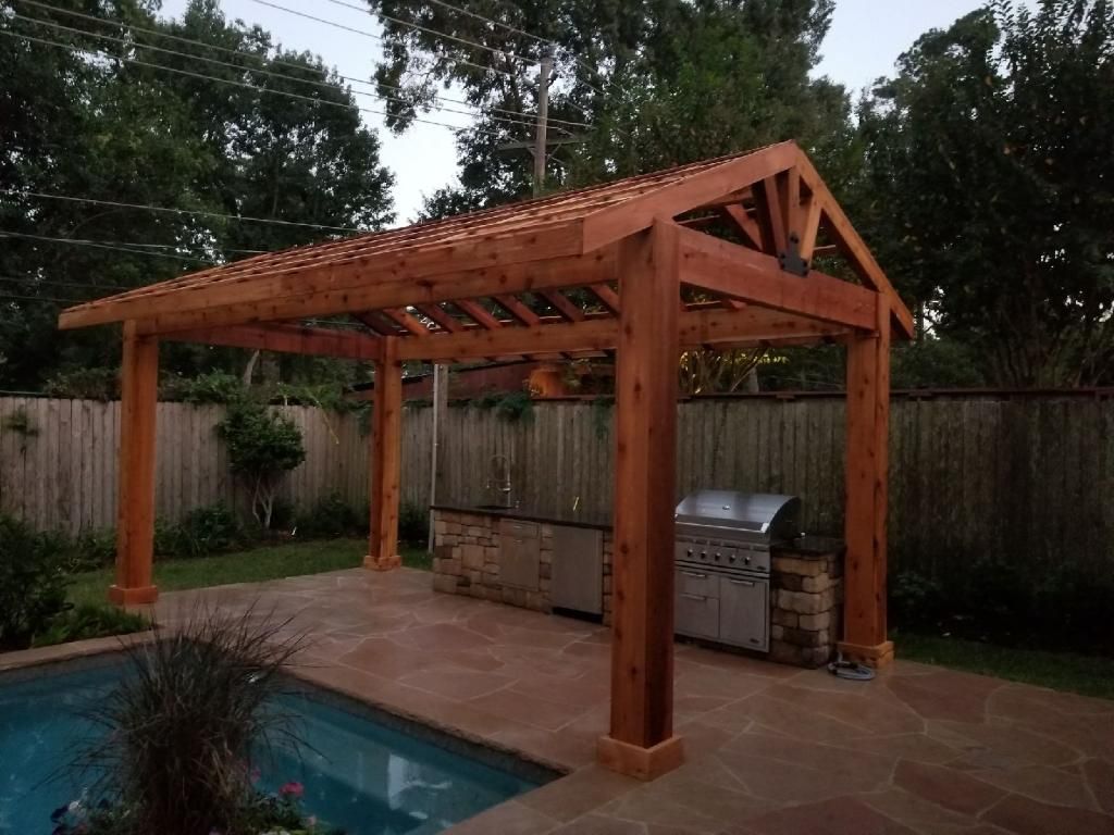 Wooden pergola over a poolside patio with built-in grill and privacy fence