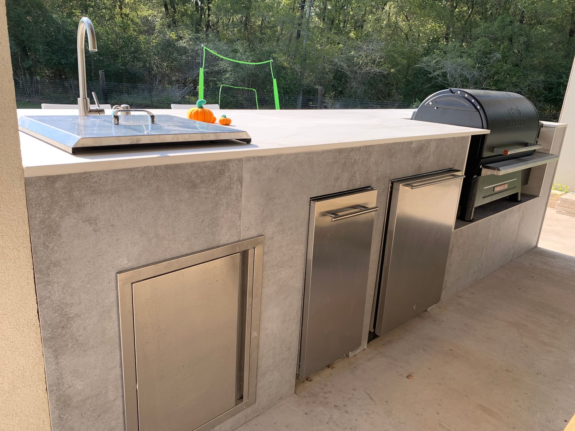 Outdoor kitchen with a stainless grill, sink, and beverage fridge on a concrete countertop