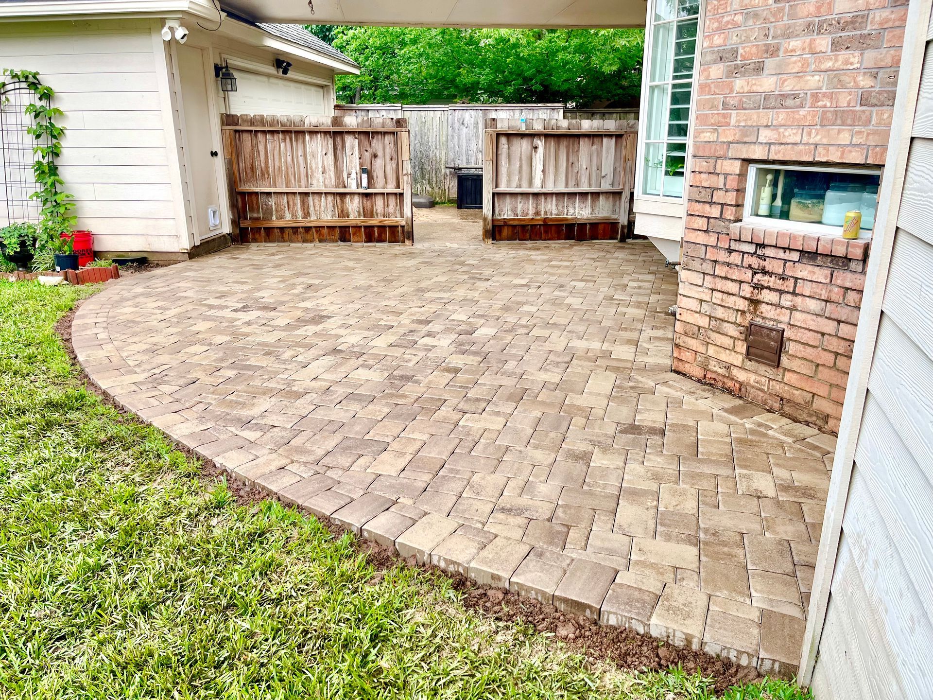 Brick paver patio with curved edge, wooden gates, brick wall, and green lawn under a covered area