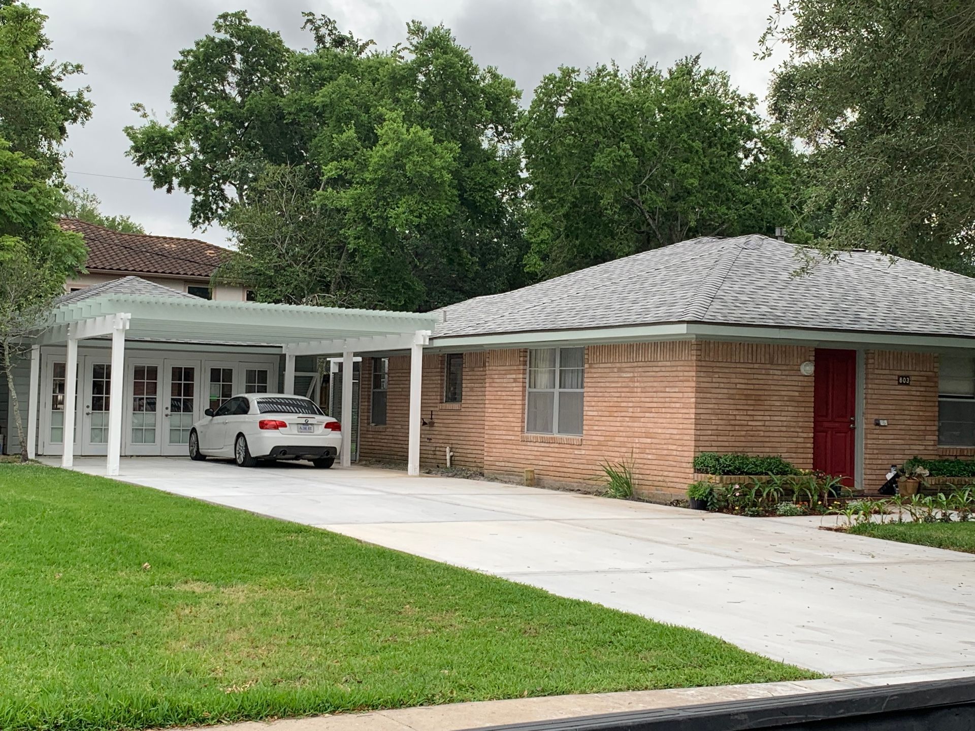 Suburban house with a car parked under a white carport and a wide concrete driveway