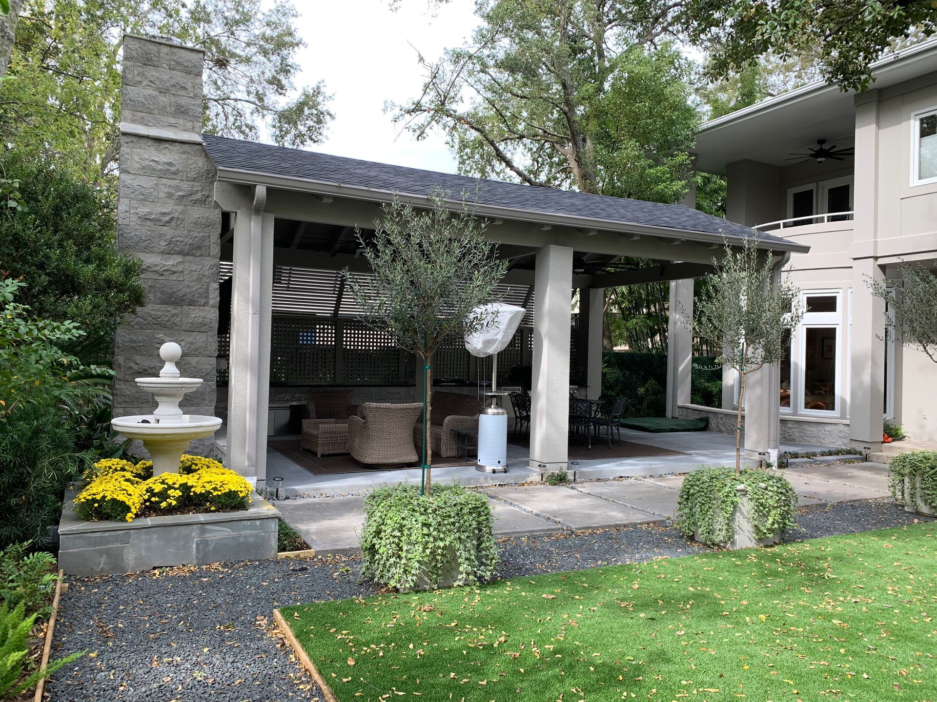 Covered patio with white columns, stone fountain, and yellow flowers beside a green lawn