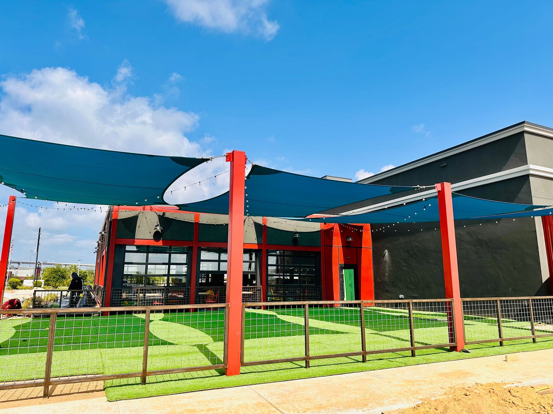 Modern building entrance with red columns, blue shade sails, and a grassy foreground