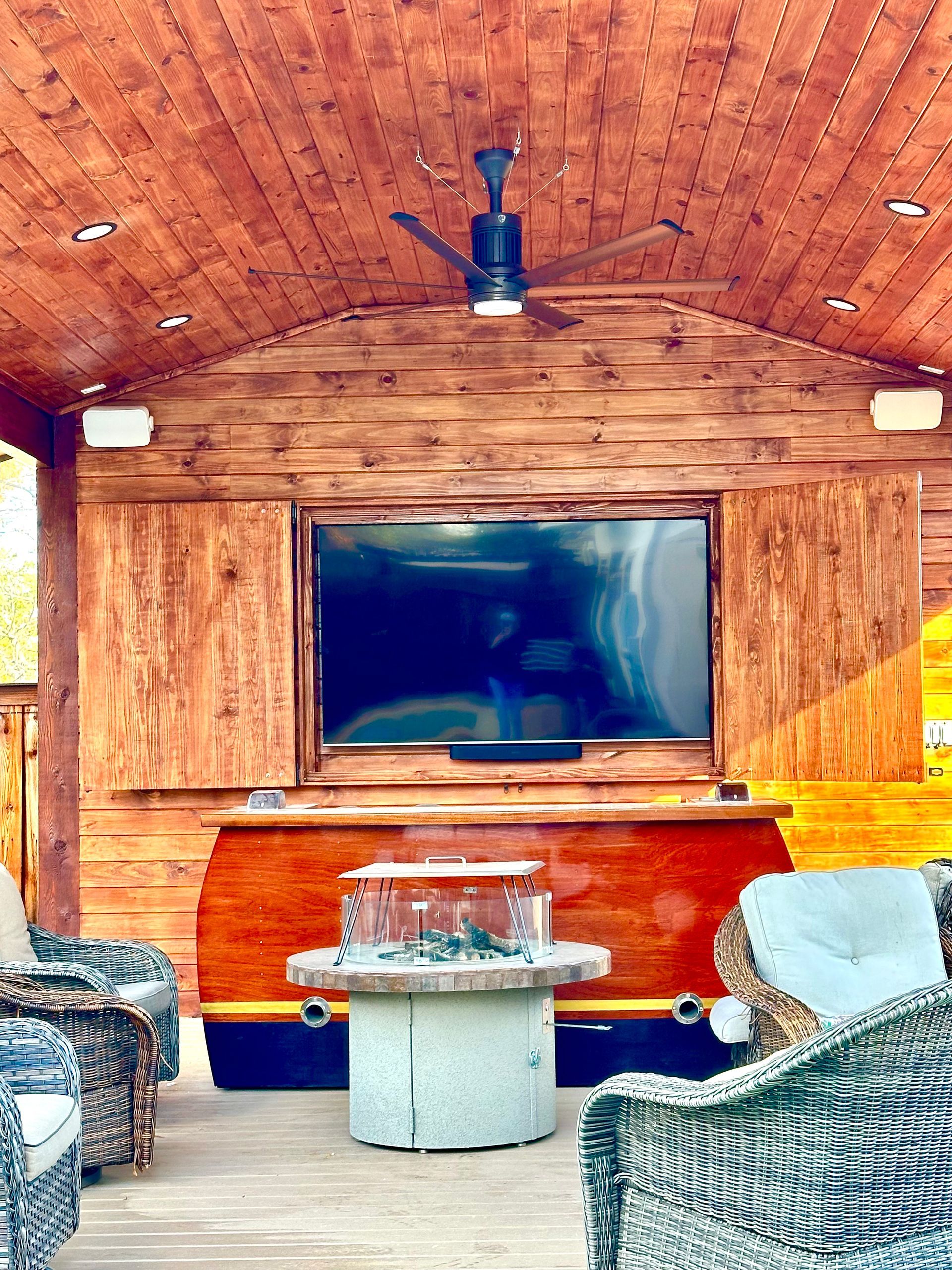 Cozy wooden patio with TV, ceiling fan, and wicker seating around a small round table.