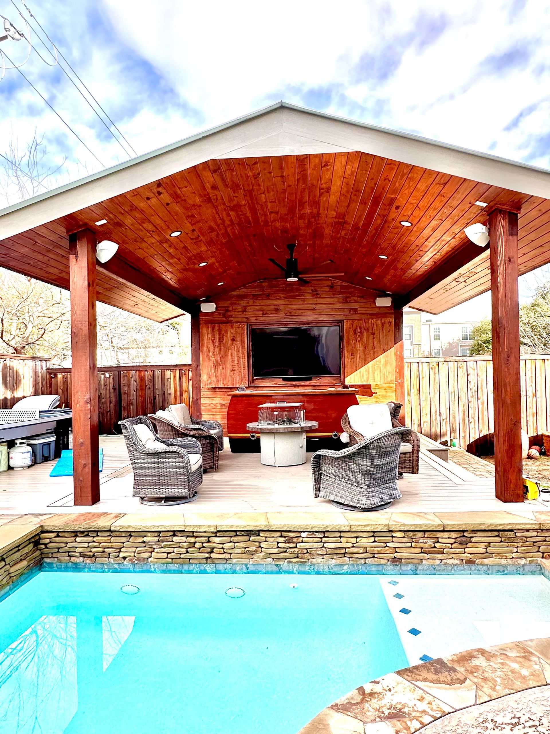 Covered patio with outdoor TV, seating, grill, and pool in front