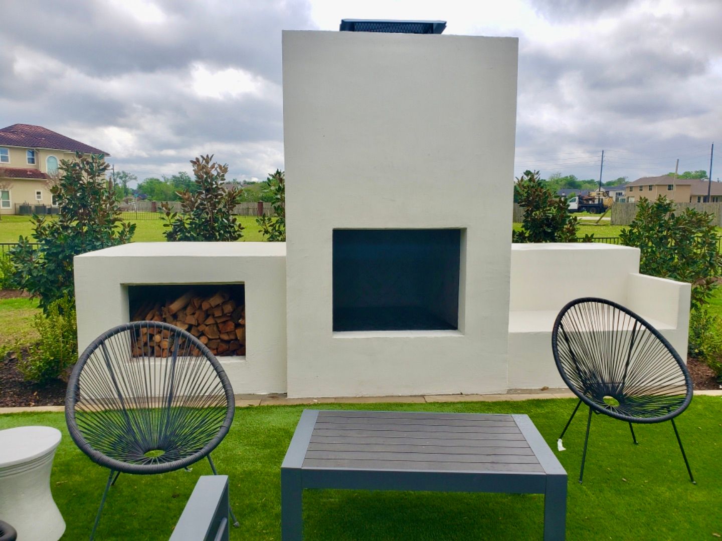 Modern patio with black chairs, table, and white outdoor fireplace against a grassy yard.