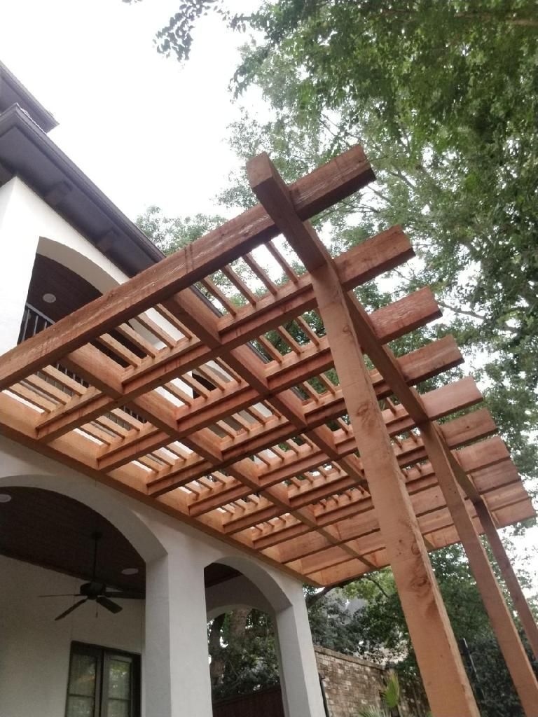 Wooden pergola over a white house patio, viewed from below with trees overhead.