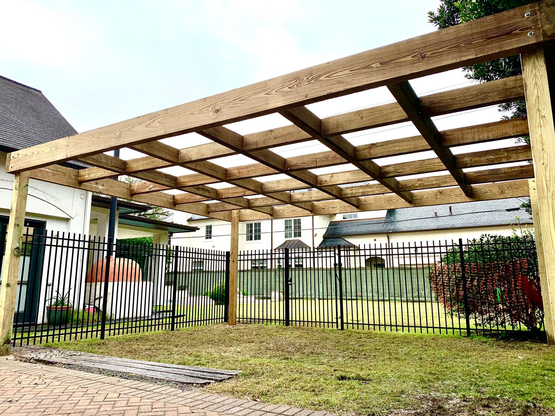 Wooden pergola carport beside a lawn and metal fence in a residential yard