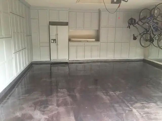 Empty garage with a glossy dark epoxy floor and white paneled walls.