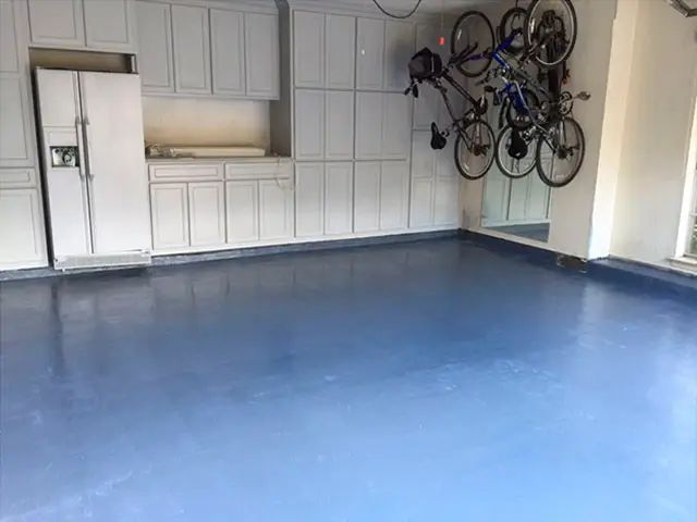 Empty garage with a blue floor, white cabinets, and several bicycles mounted on the wall.