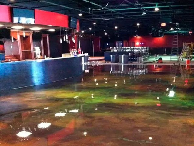 Empty indoor venue with a glossy wet floor, red bar area, and scattered reflections of lights.