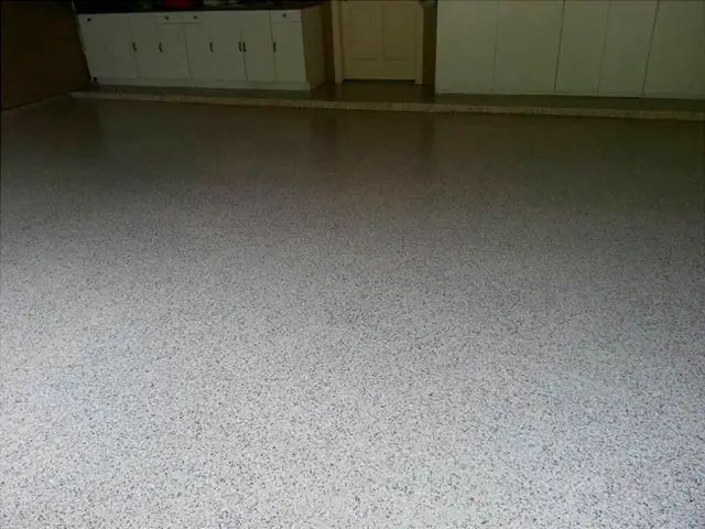 Empty speckled floor in a dimly lit room with cabinets along the back wall