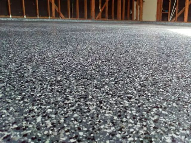Close-up of a speckled gray carpeted floor with a wooden wall in the background