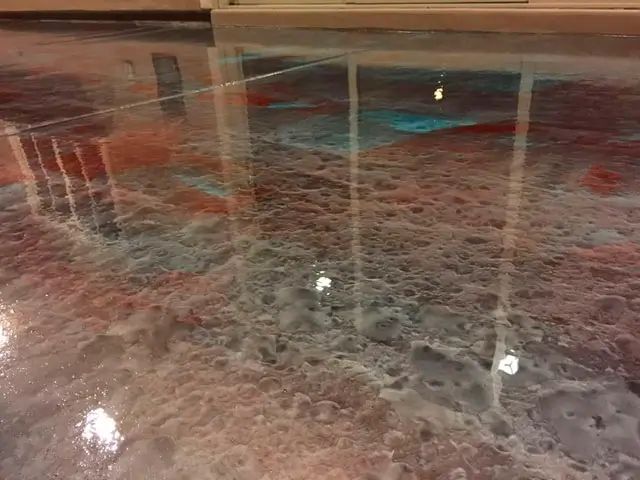 Flooded indoor floor reflecting lights and railings, with water covering the surface.