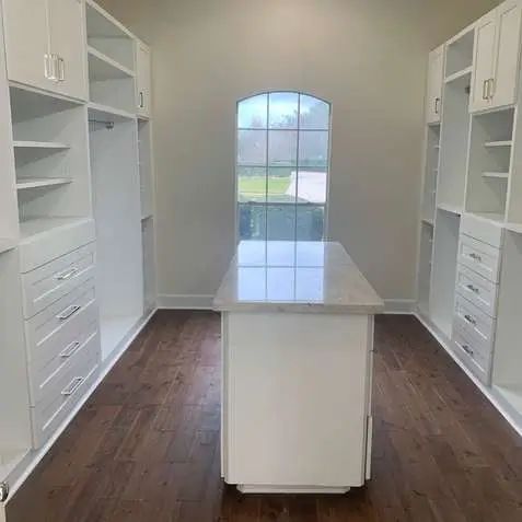 Walk-in closet with white built-in shelves, drawers, and a central island on dark wood floors.