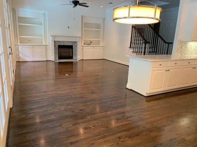Empty living room with hardwood floors, fireplace, ceiling fan, and white built-in cabinets