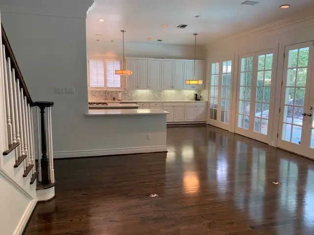 Empty open-plan kitchen and dining area with dark hardwood floors, white cabinets, and French doors.