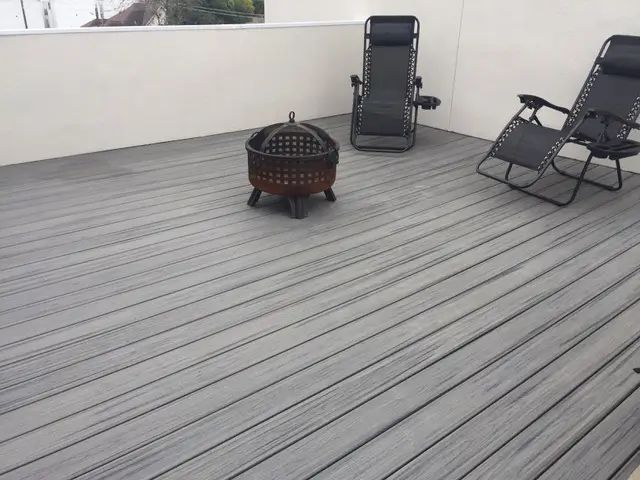 Rooftop deck with two black lounge chairs and a round fire pit on gray decking.