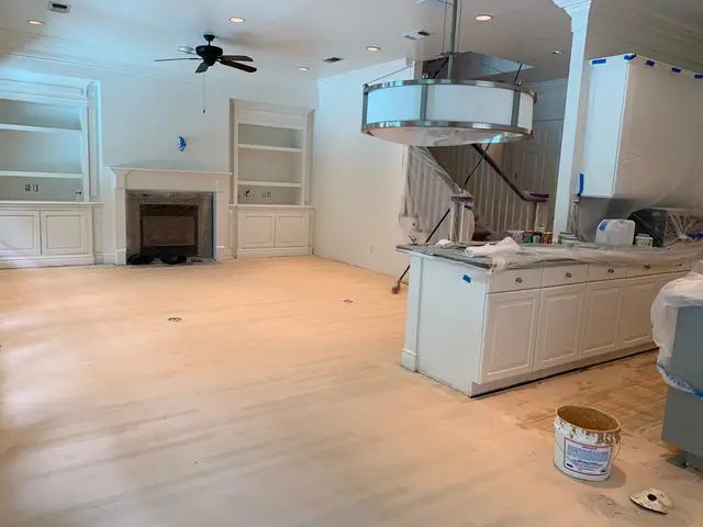 Empty renovated kitchen with light wood floors, white cabinets, island, and a ceiling fan dangling above.