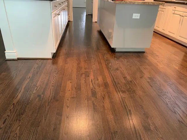 Kitchen with dark wood flooring and white cabinets, viewed from a central walkway
