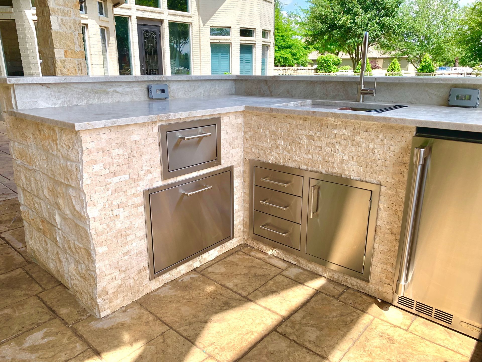 Stone outdoor service counter with stainless steel doors and vents in a sunlit patio area
