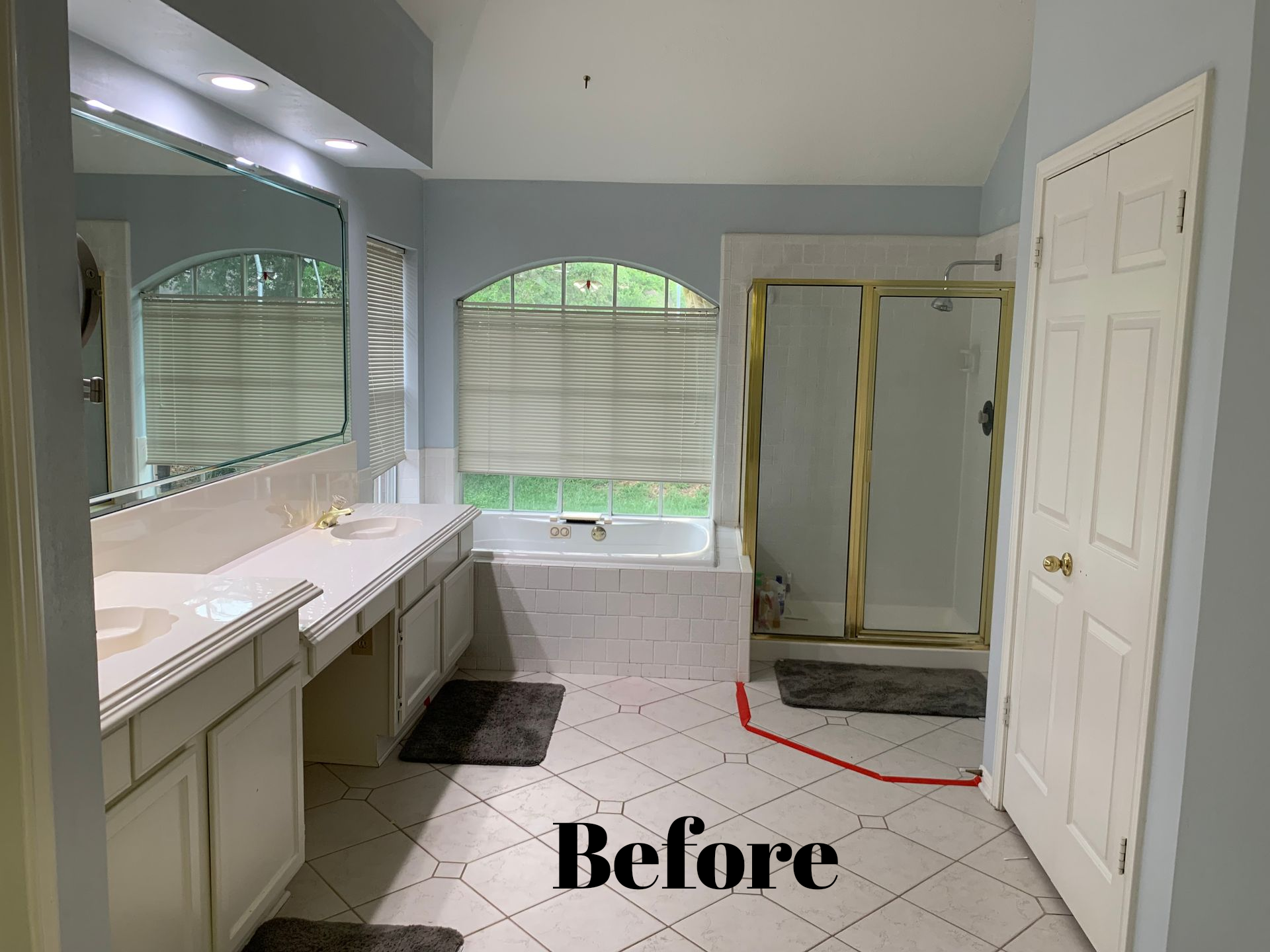 Bathroom interior with white vanity, arched windows, tub, shower doors, and large “Before” text.