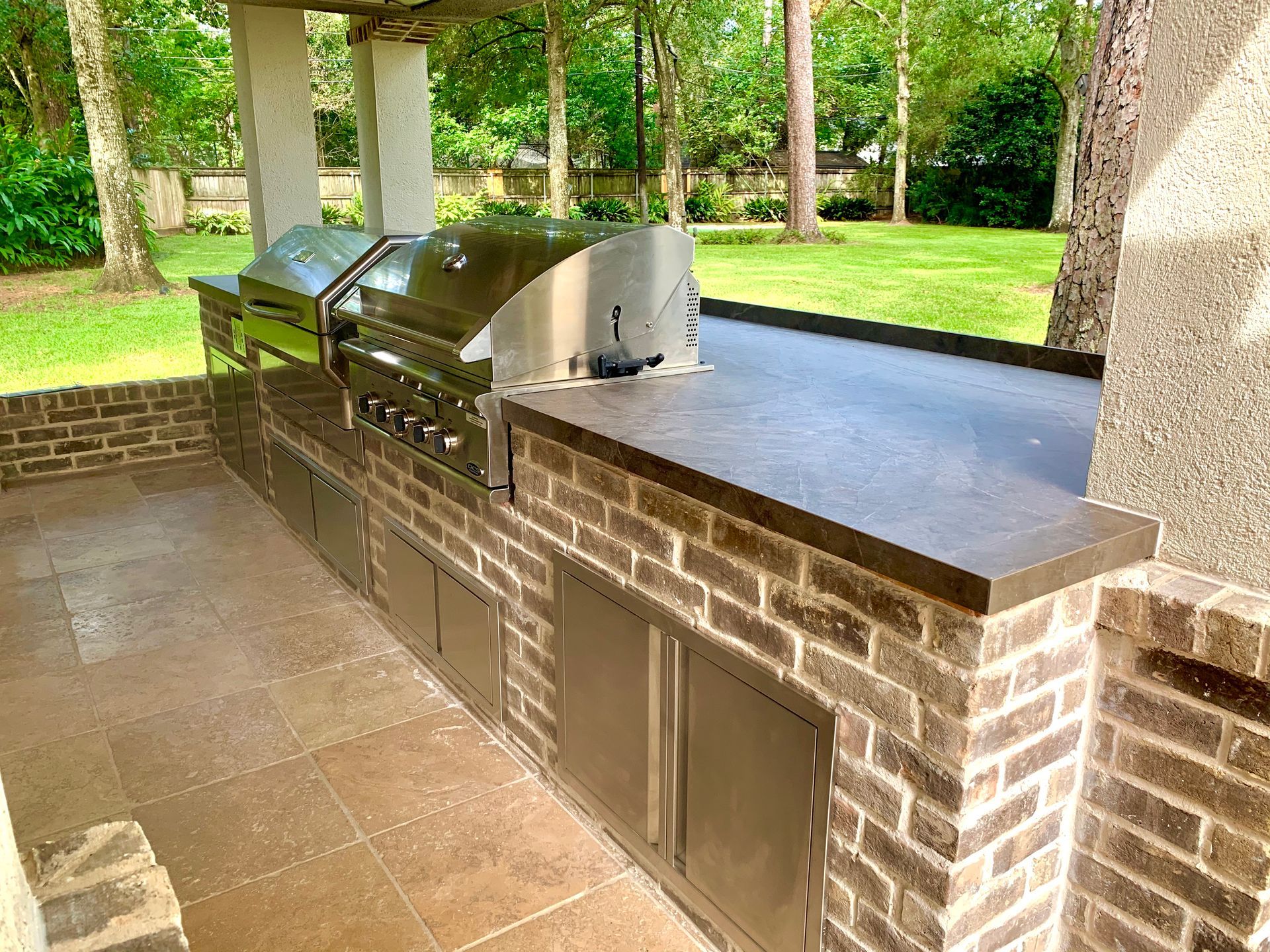 Outdoor brick grill counter under a pavilion with a stainless steel barbecue and sink