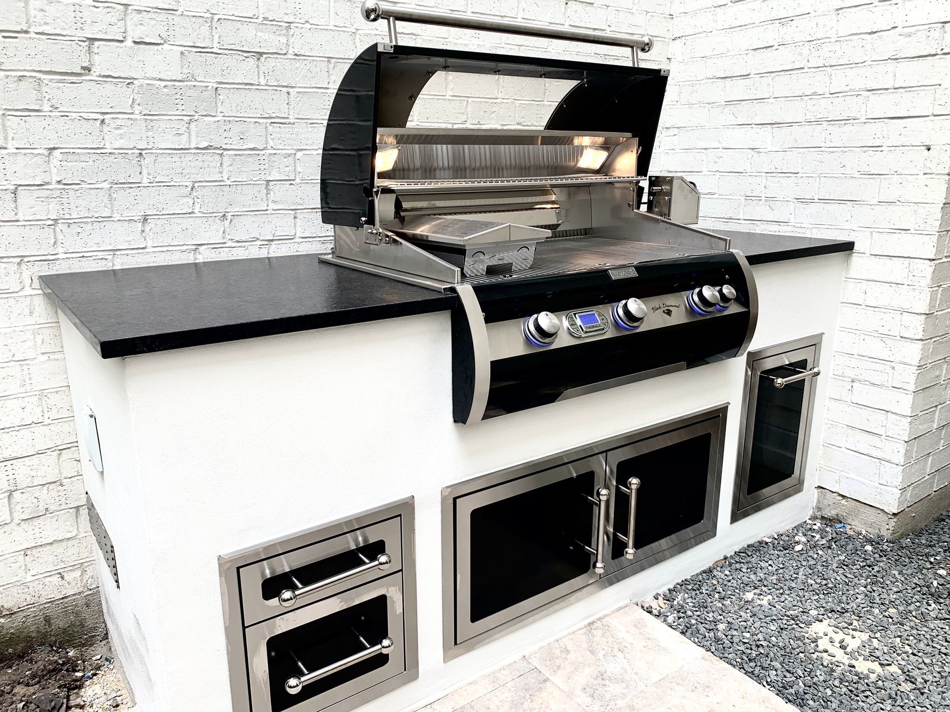 Outdoor built-in gas grill with black countertop and white base against a brick wall