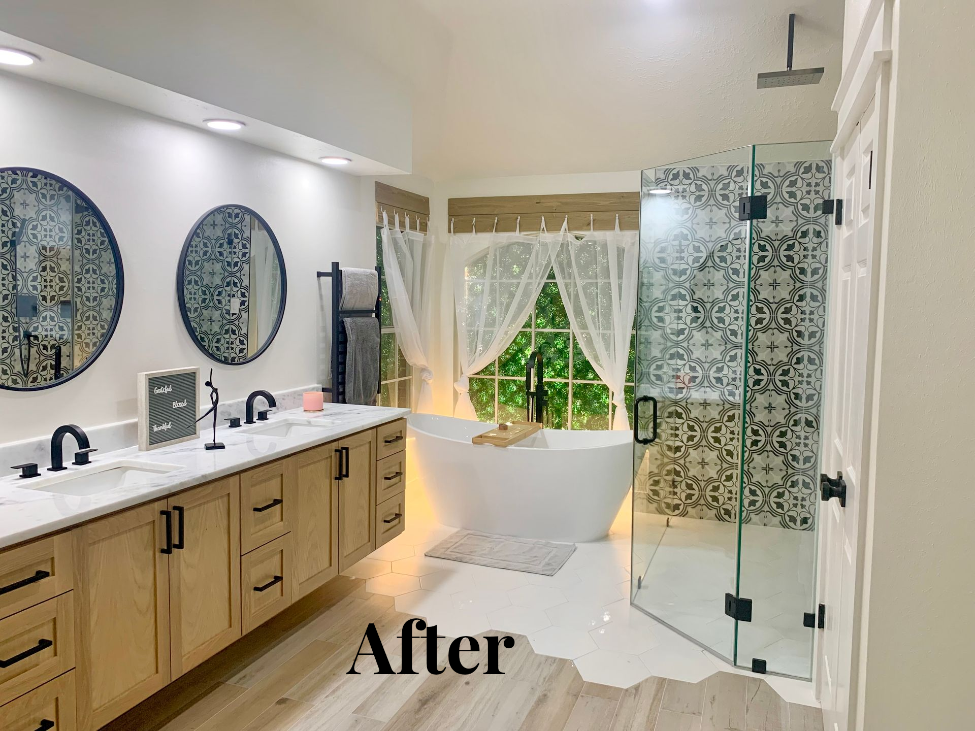 Bright modern bathroom with wood vanity, twin mirrors, glass shower, and freestanding tub by a window.