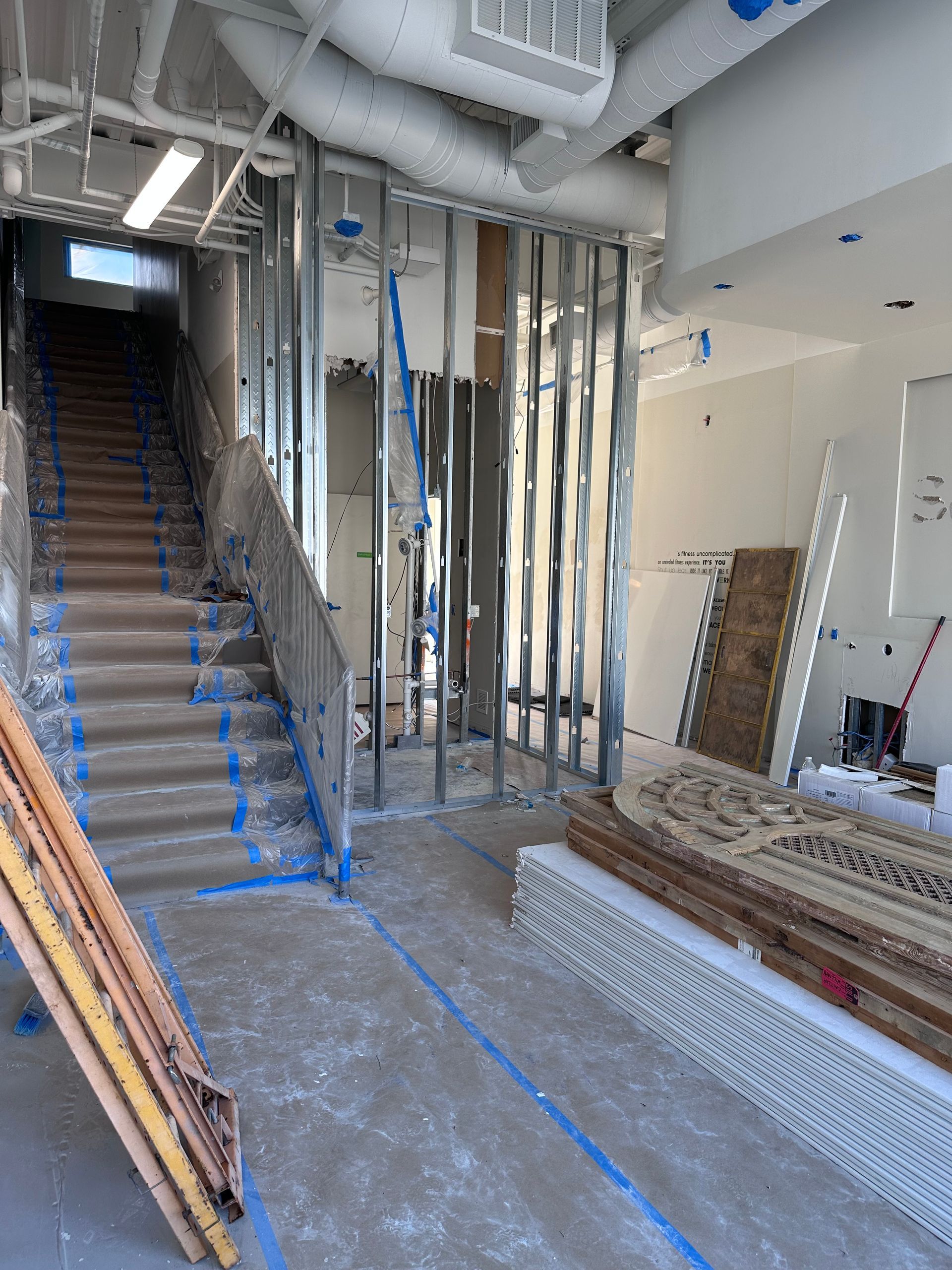 Interior renovation site with exposed framing, blue-marked stairwell, and stacked materials.