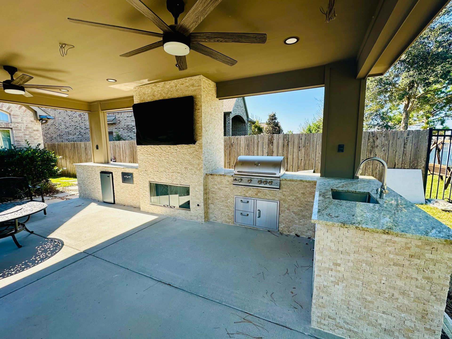 Covered outdoor patio with built-in stone grill, ceiling fan, and granite counters under a pergola.