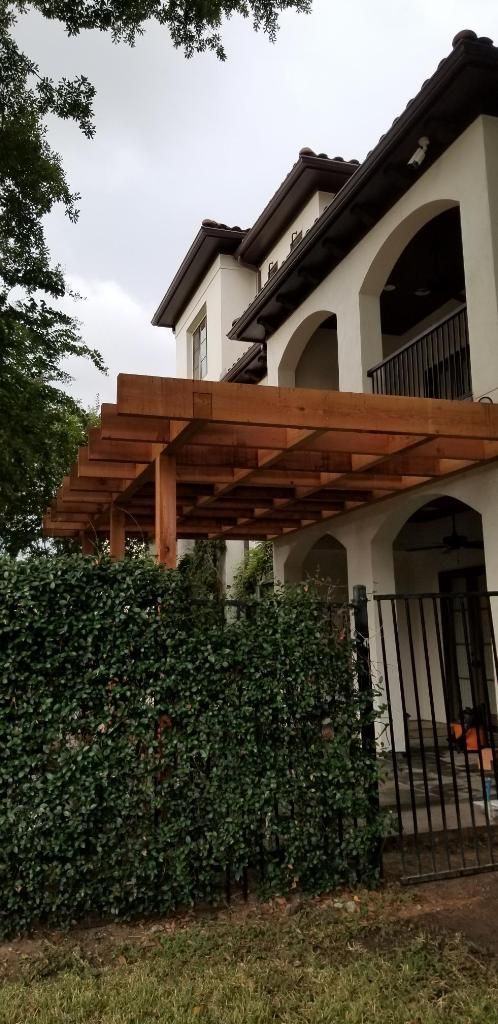 White two-story house with arched balconies and a wooden pergola over a vine-covered fence