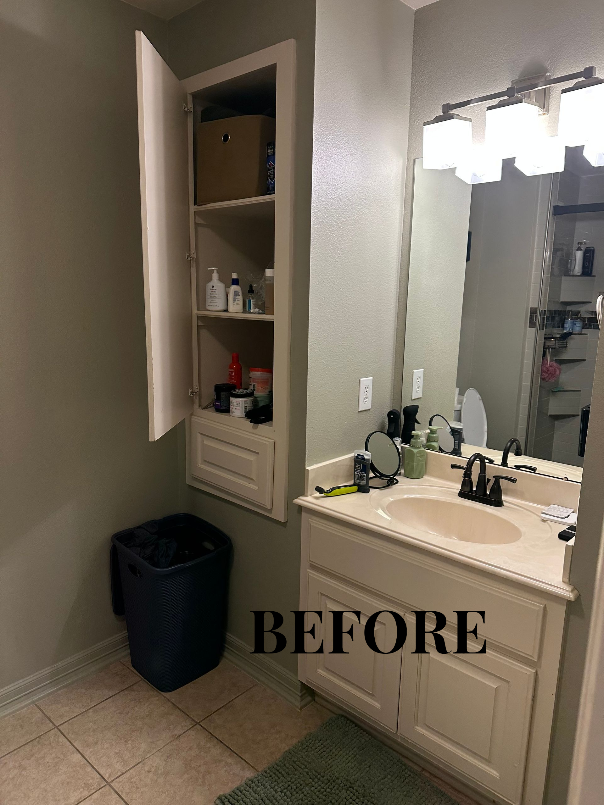Small bathroom with open wall cabinet, vanity, mirror, and trash bin; labeled “BEFORE.”