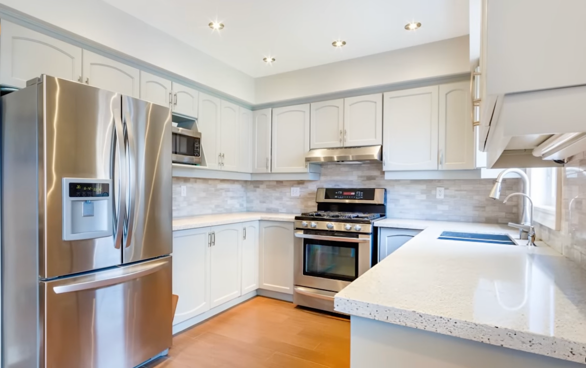 Bright white kitchen with stainless steel appliances, marble counters, and light cabinetry
