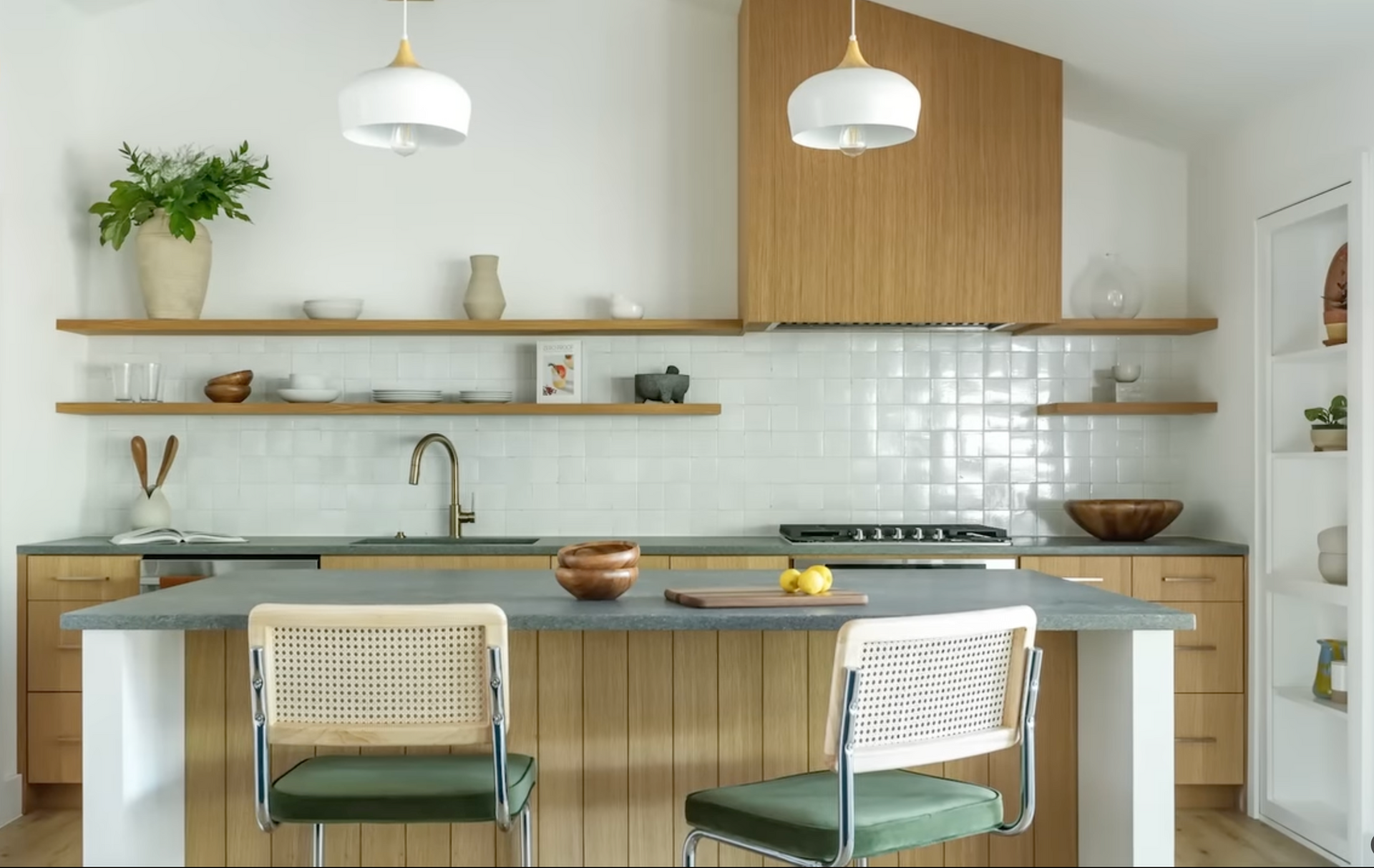 Modern kitchen with wooden cabinets, white tile backsplash, open shelves, and two green chairs at a central island