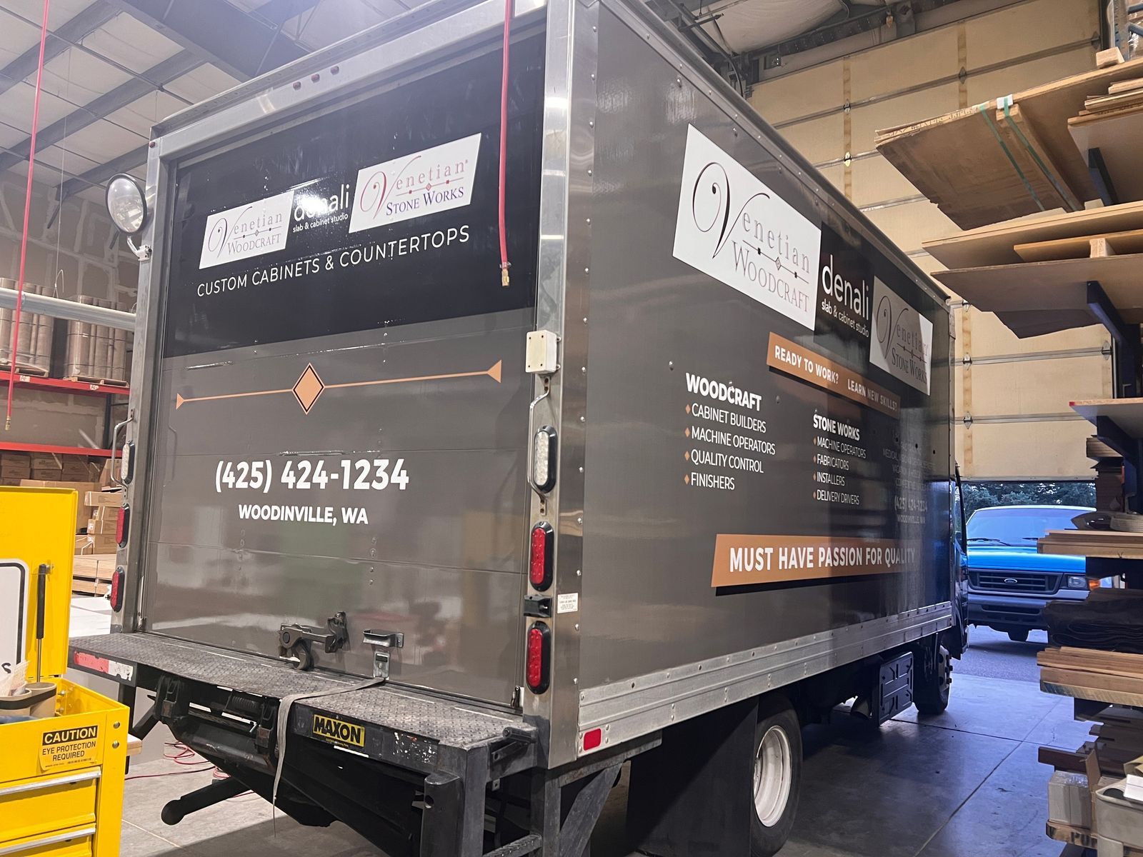 Black delivery box truck in a warehouse, with company branding and phone number on the side.