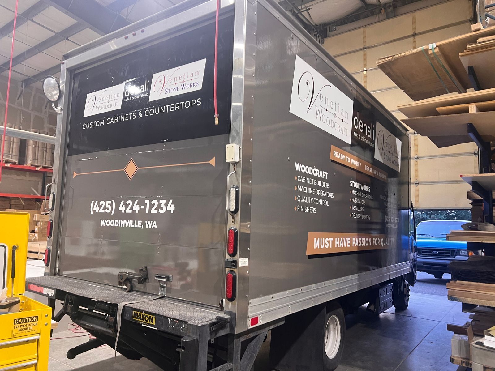 Black box truck parked indoors in a warehouse, with company logos and phone number on the back.