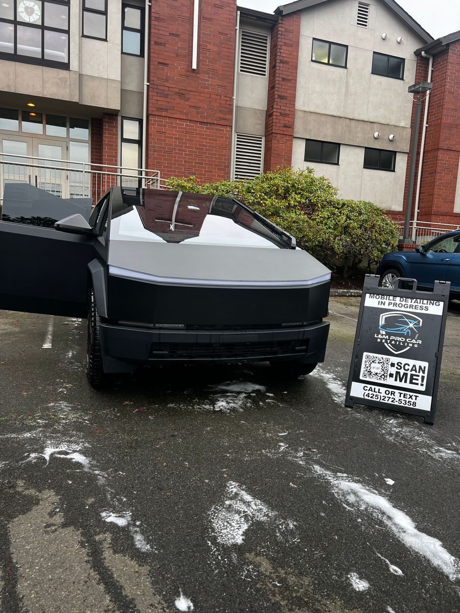 Black Cybertruck parked in front of brick apartment buildings on a wet street, with a sign beside it.
