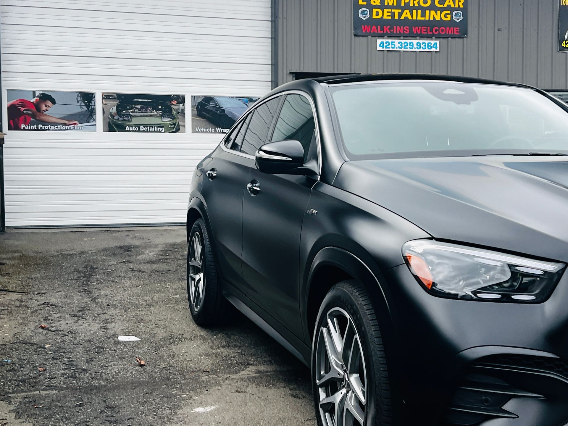 Black sedan parked outside an auto detail shop with garage doors and signs in the background