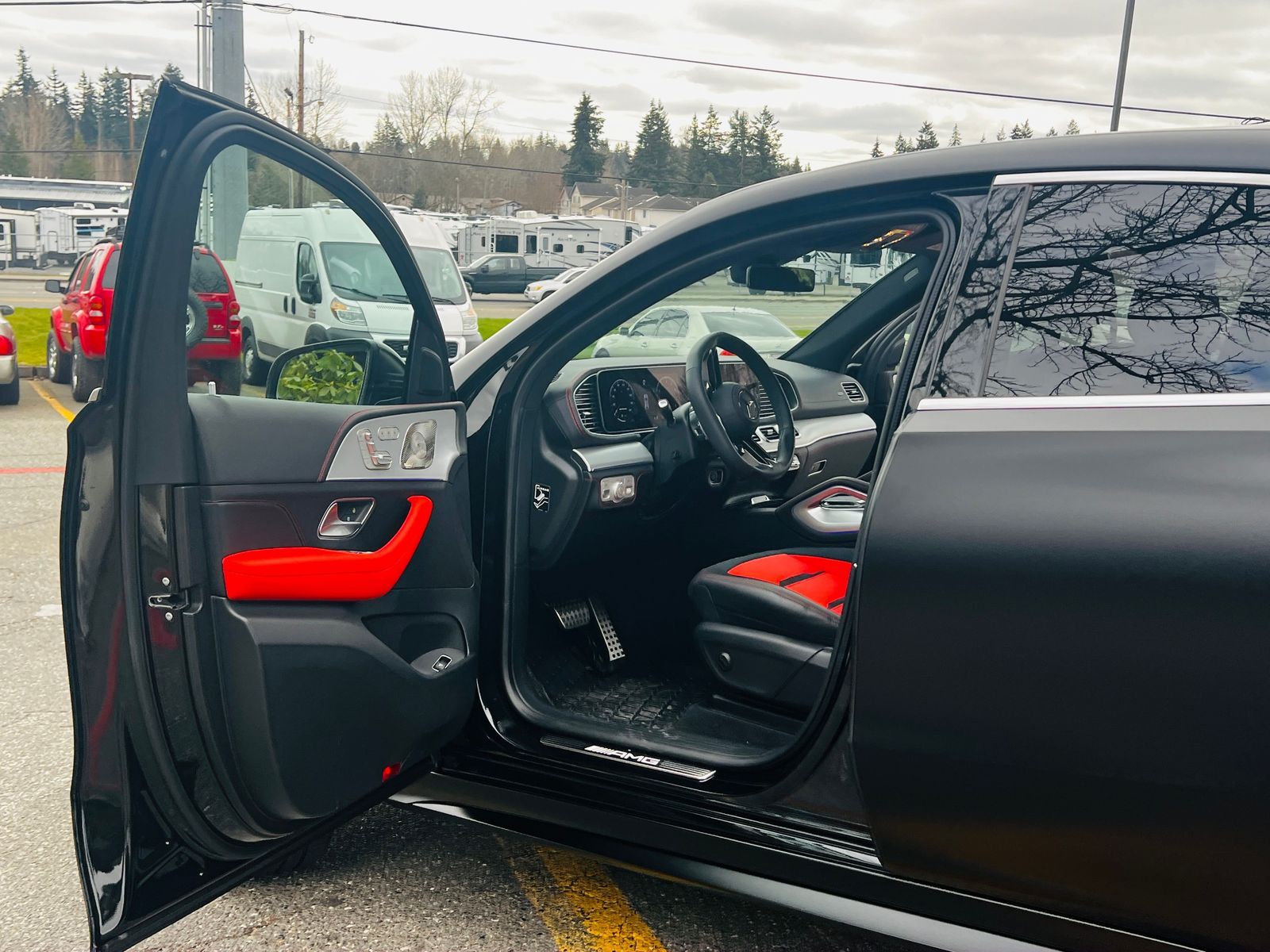 Open car door revealing black and red leather interior at a dealership lot.