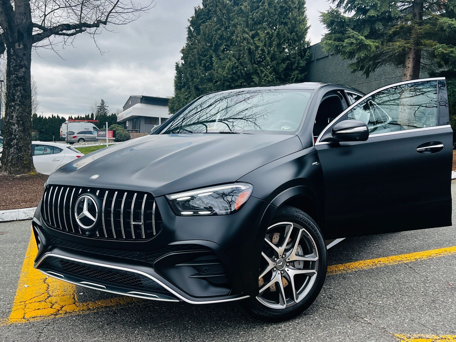 Black Mercedes SUV parked at an angle in a lot, driver door open on a rainy day