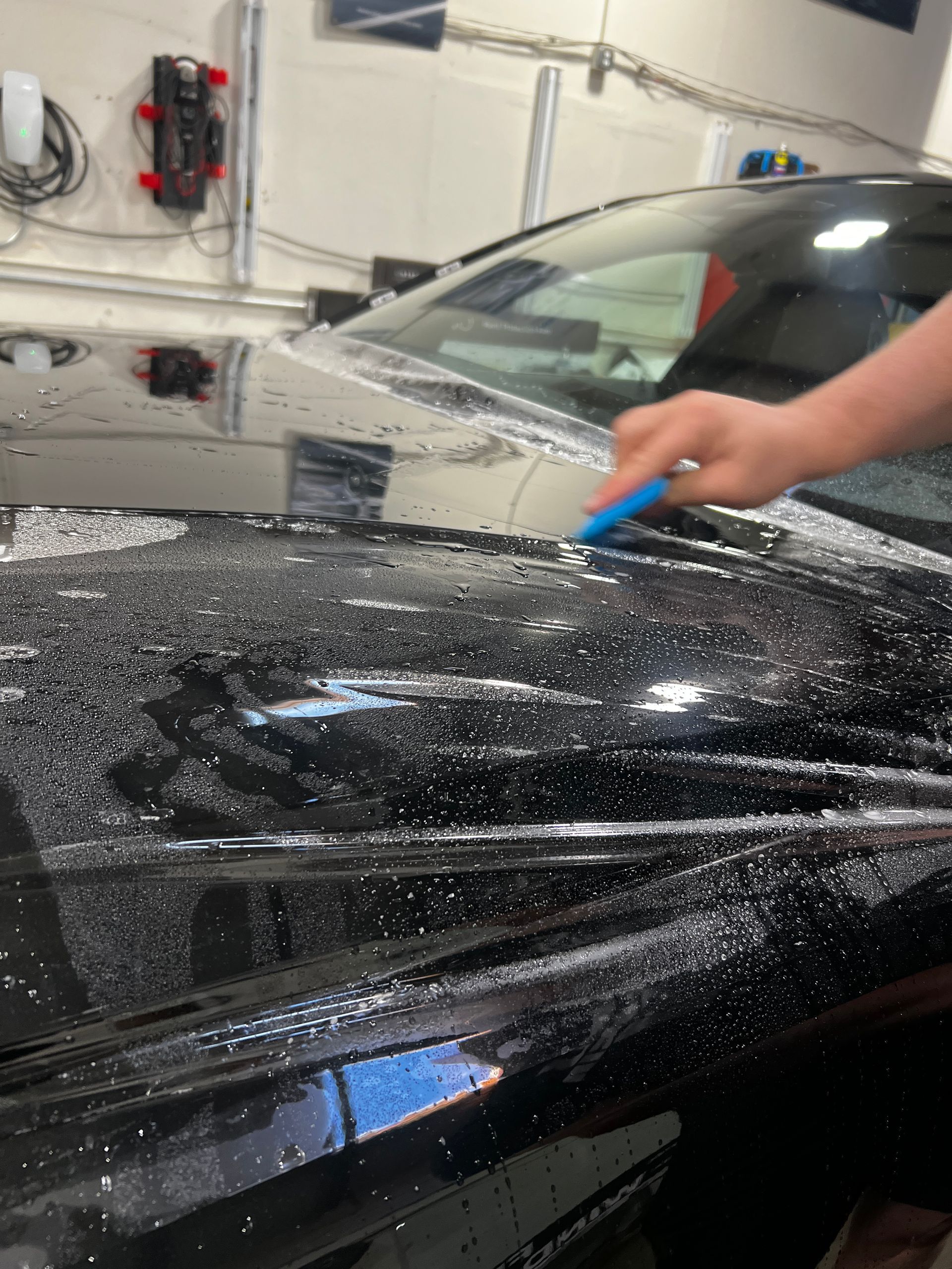 Person scrubbing a black car hood with a blue sponge in a car wash