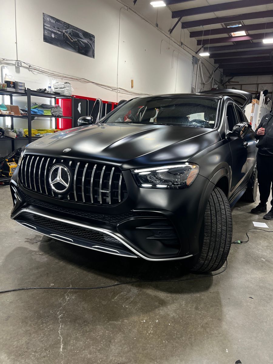 Black Mercedes SUV in an auto shop, shown from the front on a wet floor, with a person standing beside it