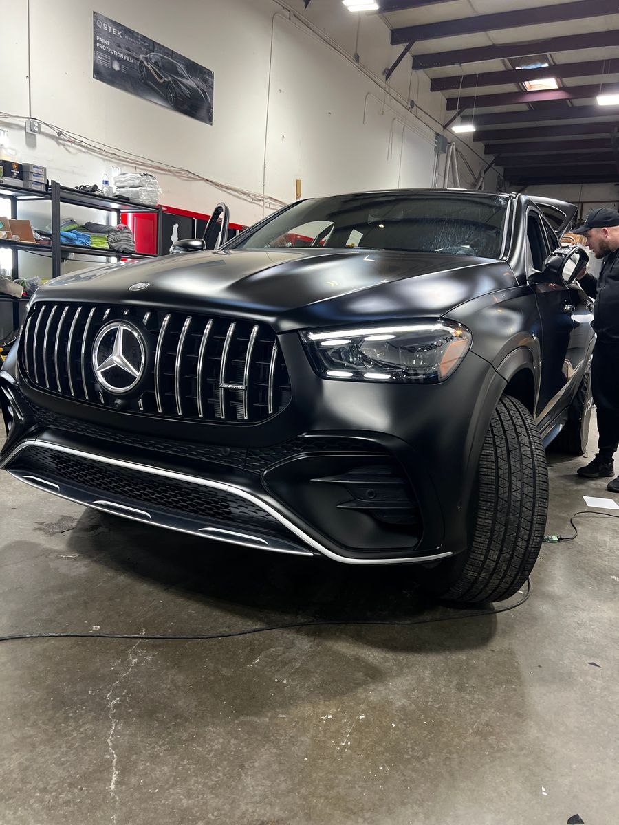 Black Mercedes-Benz SUV in an auto shop, front view with headlights on and front wheel turned.