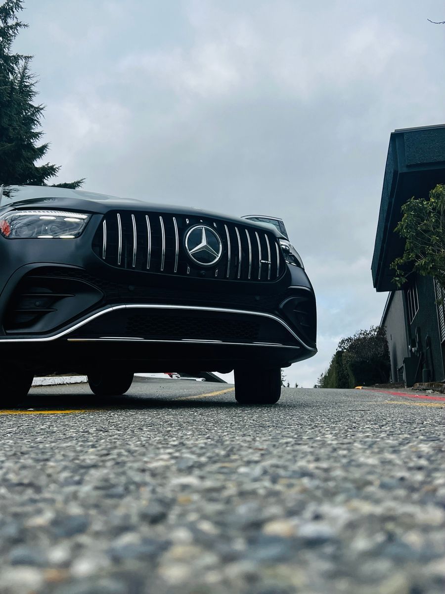 Low-angle view of a black Mercedes SUV parked on a road under a cloudy sky.