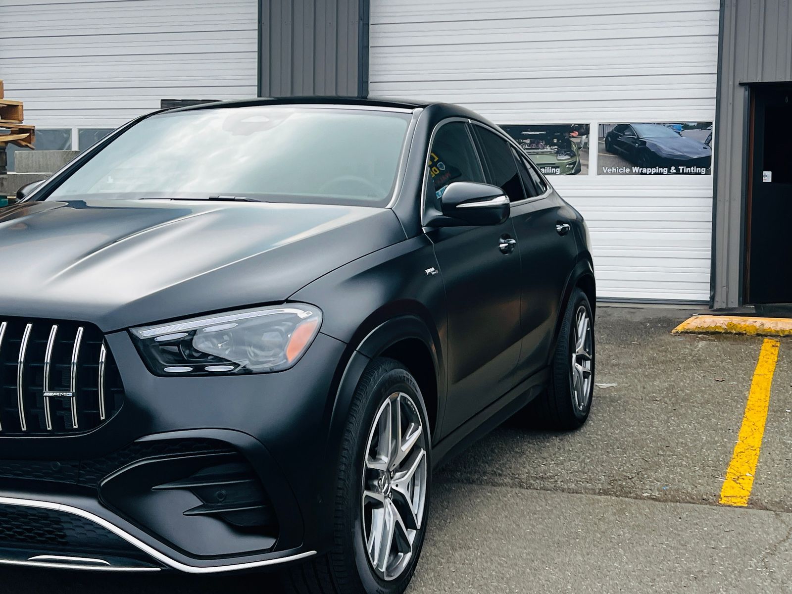 Dark gray luxury SUV parked outside a garage beside a yellow curb line