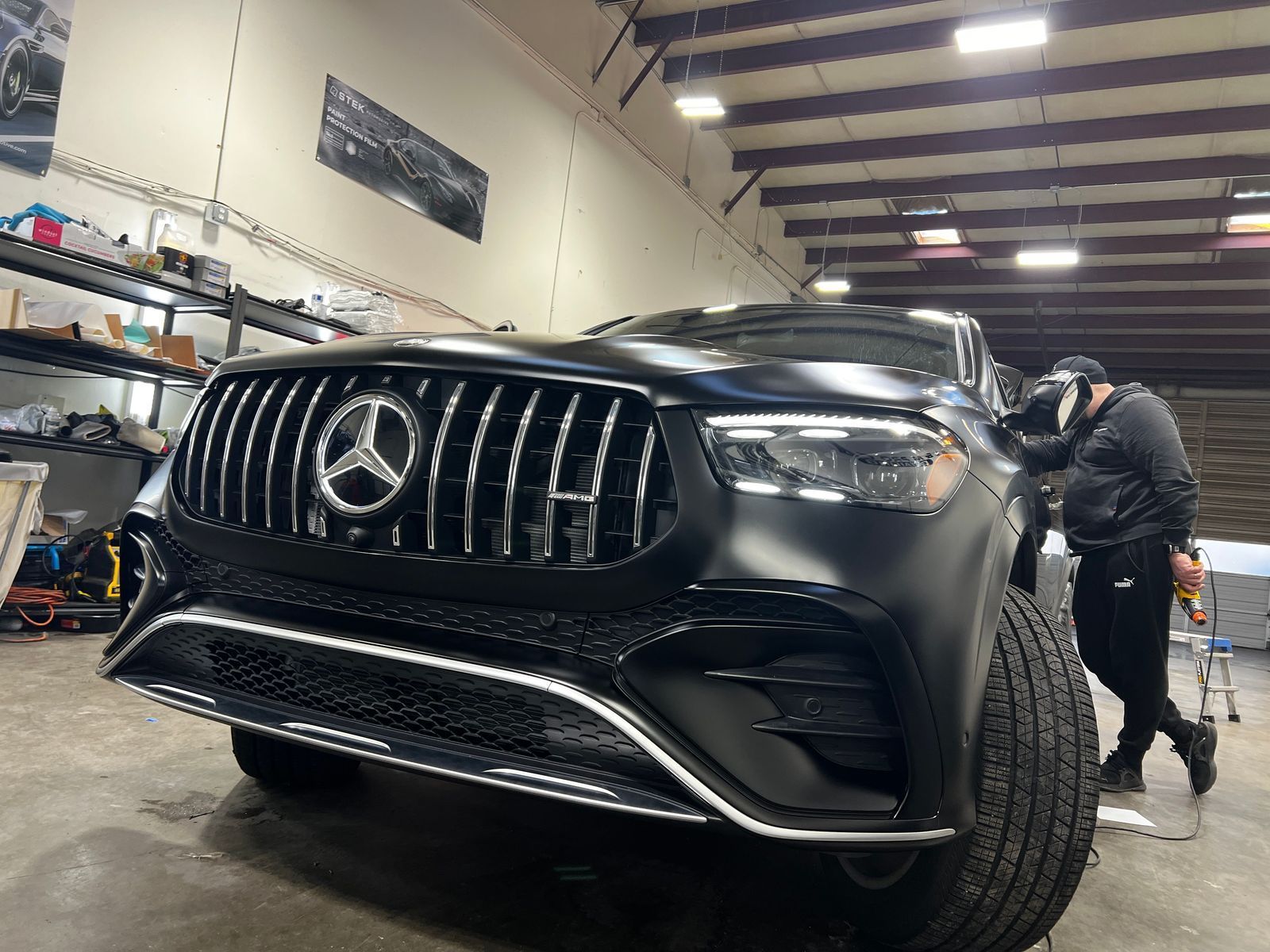 Black Mercedes SUV in an auto shop, with a mechanic working on the front right wheel.