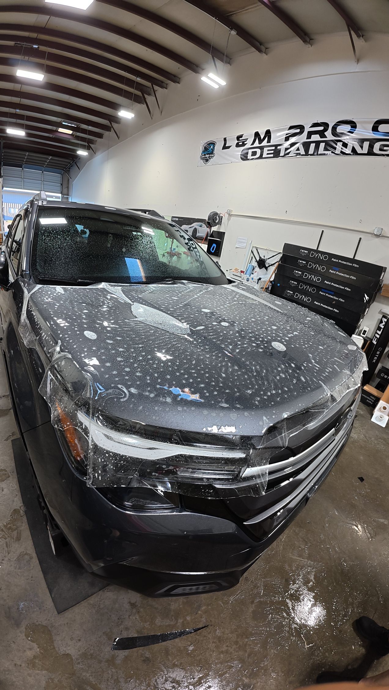 Dark gray SUV in a garage, front view, with shattered windshield and water droplets on the hood.