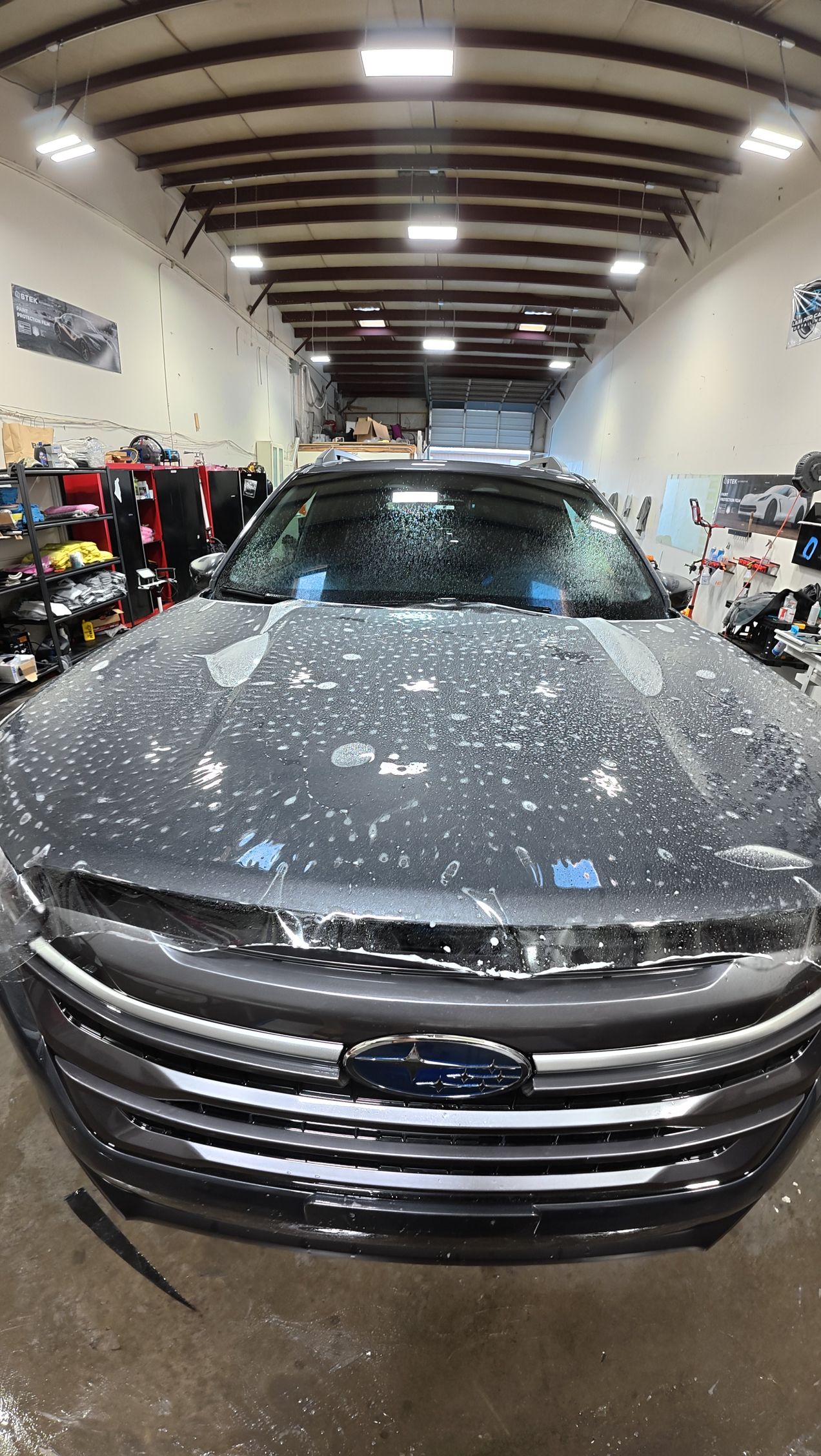 Gray SUV in a car wash bay, covered in soap suds with the front grille visible.