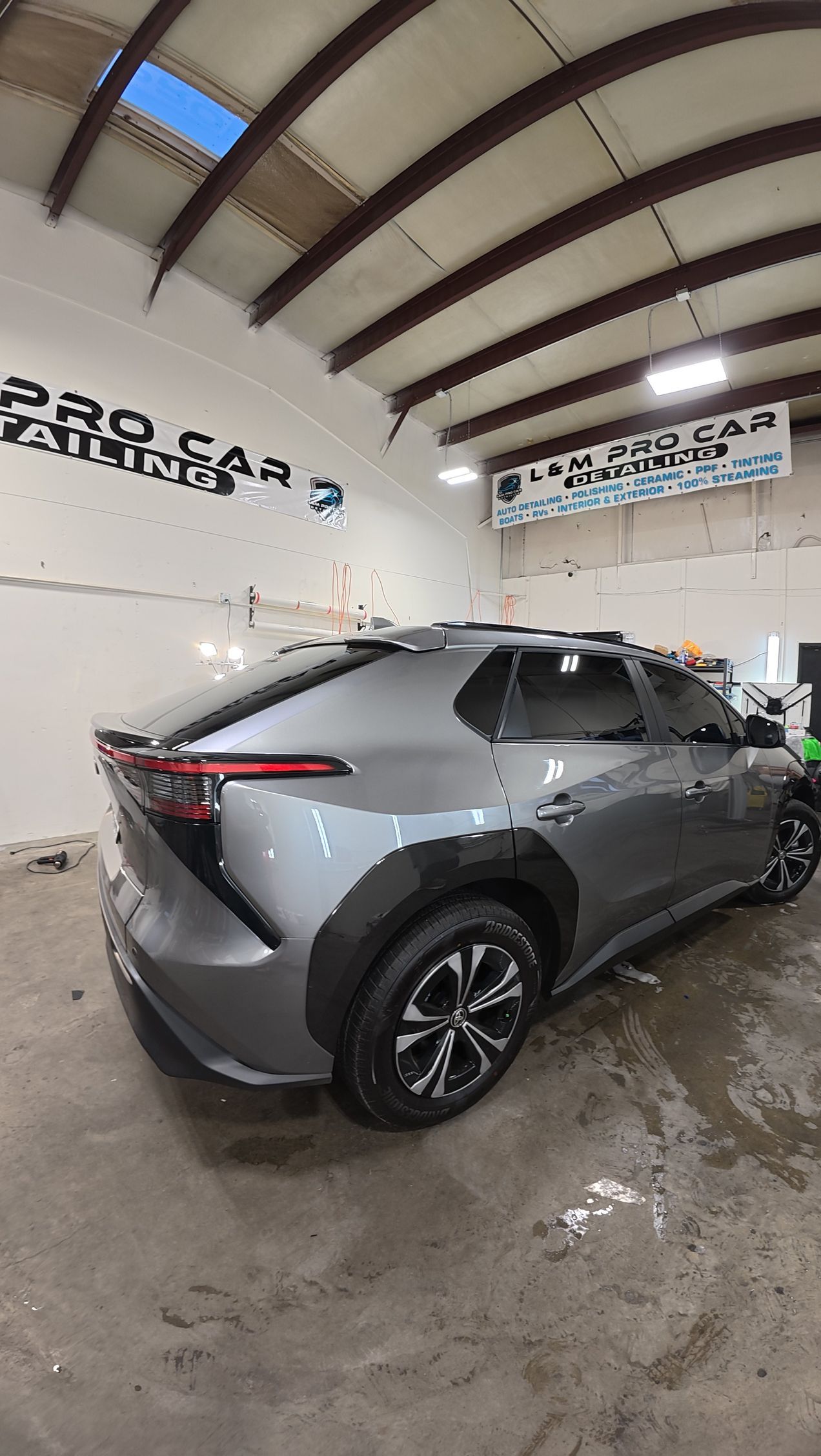 Gray SUV parked inside a wet car wash bay under a curved metal roof.ccccccccccccc