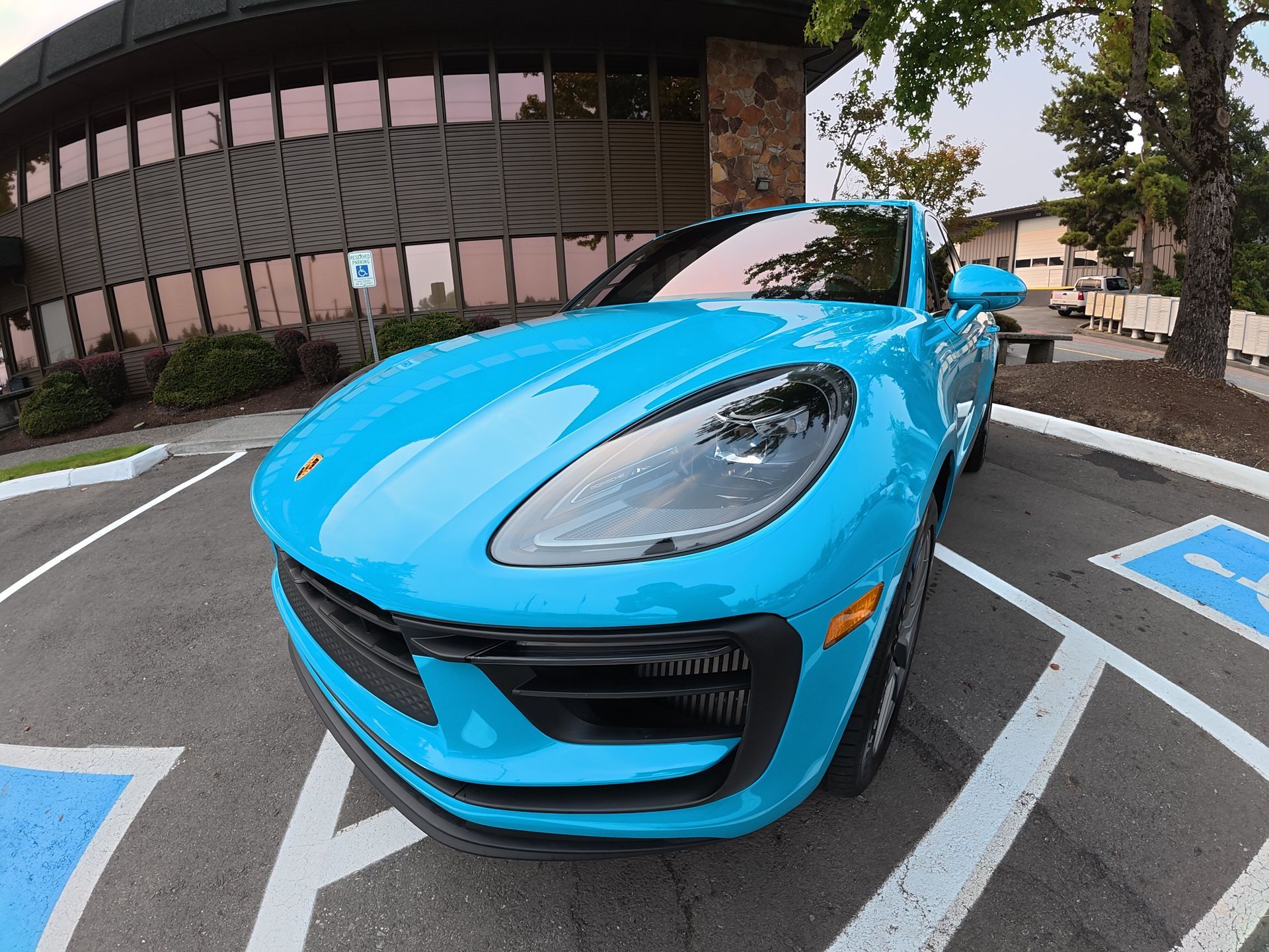 Bright blue sports car parked in a marked lot outside a glass building